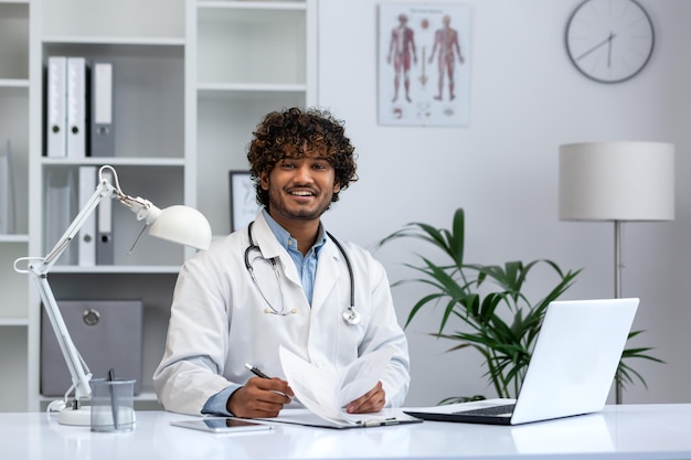 Retrato de jovem médico hispânico bem-sucedido dentro da clínica, sorrindo e olhando para o médico da câmera