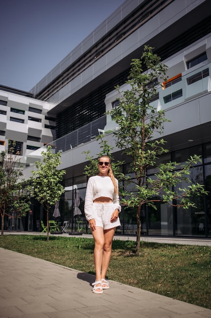 Retrato de jovem modelo de empresária moderna sexy mulher bonita de terno branco posando no fundo da rua moda feminina andando ao ar livre em óculos de sol passando a faixa de pedestres da zebra