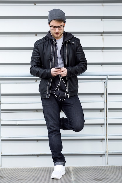 Retrato de jovem moderno usando seu telefone celular na rua.