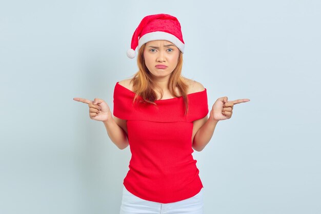 Retrato de jovem mulher asiática com vestido de natal apontando para as laterais, tendo dúvidas