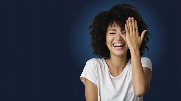 Retrato de jovem mulher bonita despreocupada com cabelo encaracolado cobre metade do rosto com a palma da mão e ri.