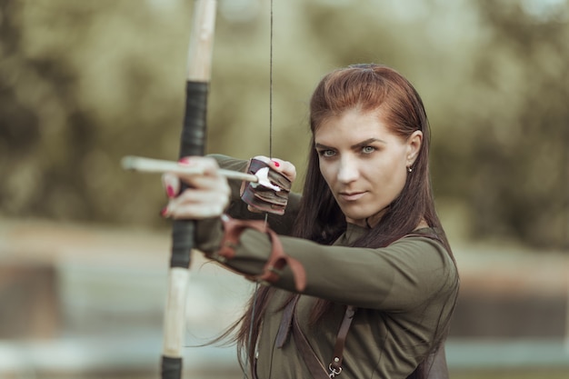 Retrato de jovem mulher com arco e flecha no fundo da floresta