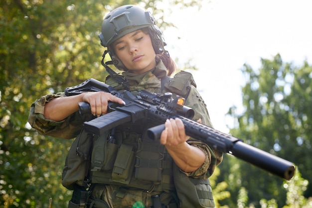 Retrato de jovem mulher com arma em traje militar ao ar livre