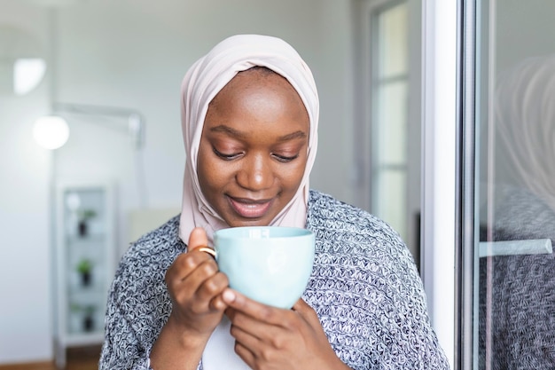 Retrato de jovem mulher muçulmana africana com o lenço de cabeça sorrindo Pérola do Oriente Mulher muçulmana sorridente vestindo hijab segurando xícara de café Mulher musulmana moderna, elegante e feliz usando um lenço de cabeza