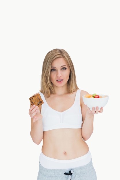 Retrato de jovem mulher segurando biscoito e tigela de frutas
