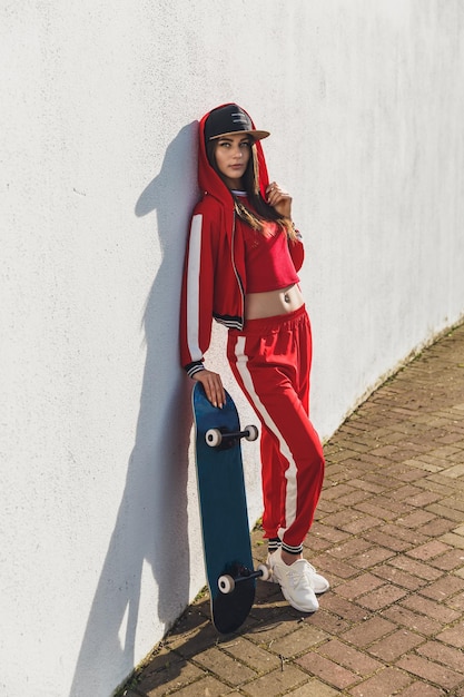 Retrato de jovem mulher vestindo chapéu preto skatista de roupas vermelhas segurando seu skate