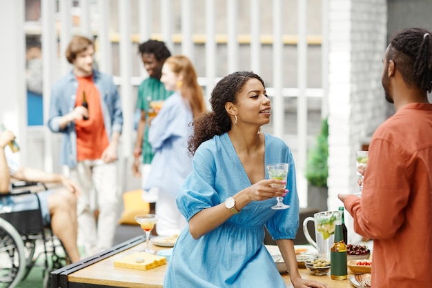 Retrato de jovem negra conversando com um amigo enquanto desfruta de bebidas na cópia da festa no terraço ao ar livre