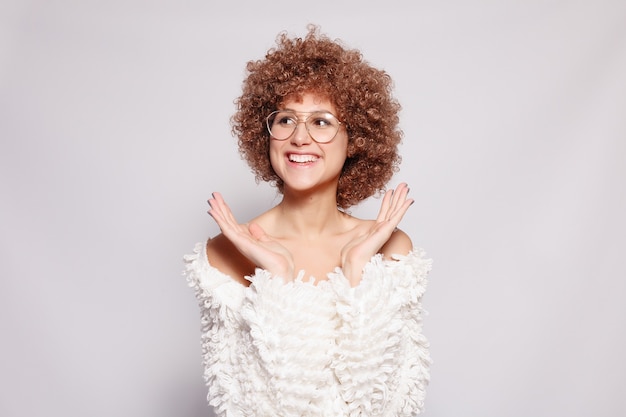 Retrato de jovem negra sorridente. Retrato de uma jovem bonita com maquiagem afro-americana de corte de cabelo e glamour. Tiro do estúdio. Garota atraente usando óculos fica surpresa