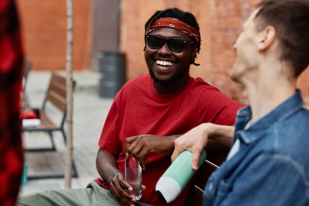 Retrato de jovem negro usando bandana e rindo alegremente enquanto conversa com amigos ou