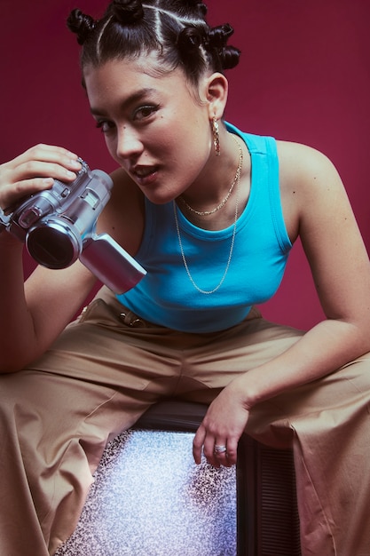 Retrato de jovem no estilo de moda dos anos 2000 posando com televisão e câmera portátil