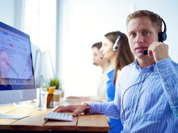 Retrato de jovem operador de call center usando fone de ouvido com colegas trabalhando em segundo plano no escritório