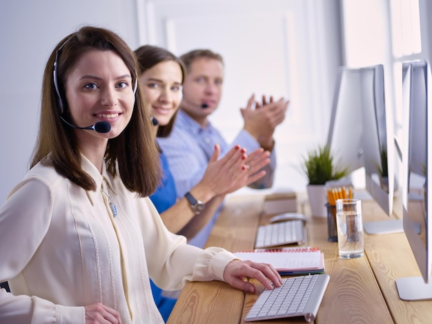 Retrato de jovem operador de call center usando fone de ouvido com colegas trabalhando em segundo plano no escritório