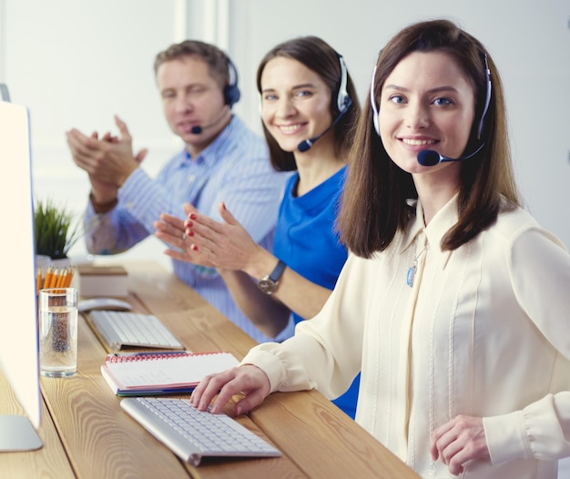 Retrato de jovem operador de call center usando fone de ouvido com colegas trabalhando em segundo plano no escritório