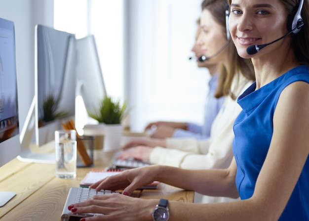 Retrato de jovem operador de call center usando fone de ouvido com colegas trabalhando em segundo plano no escritório