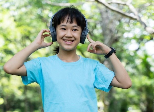 Retrato de jovem ouve música com fones de ouvido modernos no parque ao ar livre Menina pré-adolescente desfrutando de ritmos ao ouvir música com fones de ouvido sem fio