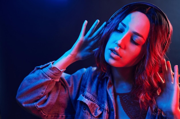 Retrato de jovem que ouve música em fones de ouvido em neon vermelho e azul no estúdio