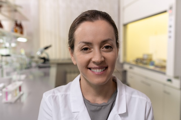 Retrato de jovem químico vestindo jaleco branco sorrindo para a câmera enquanto trabalhava no laboratório