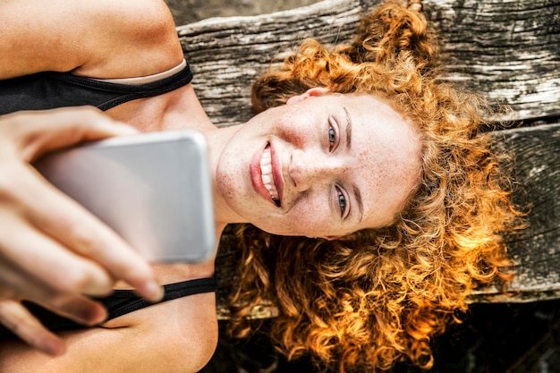 Retrato de jovem ruiva deitado no banco usando telefone celular