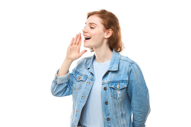 Retrato de jovem ruiva gritando nas palmas das mãos no fundo branco do estúdio conceito de notícias de informações importantes