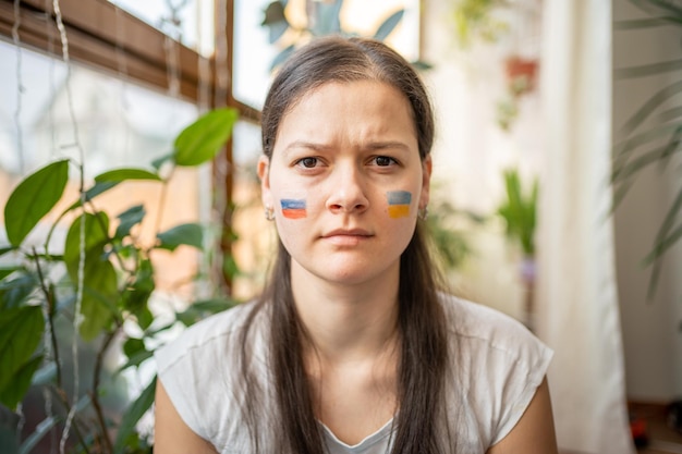 Retrato de jovem russo-ucraniano com a bandeira da ucrânia e da rússia no rosto franzindo os olhos...