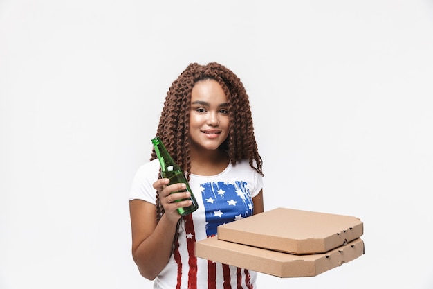 Retrato de jovem segurando caixas de pizza e uma garrafa de cerveja durante o jogo de futebol, isolado contra uma parede branca