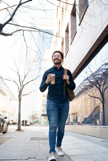 Retrato de jovem segurando uma xícara de café enquanto caminhava ao ar livre na rua. conceito urbano e estilo de vida.