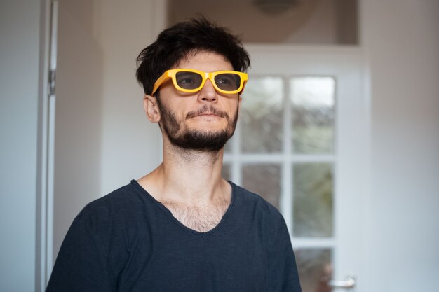 Retrato de jovem sério com óculos de sol amarelos.