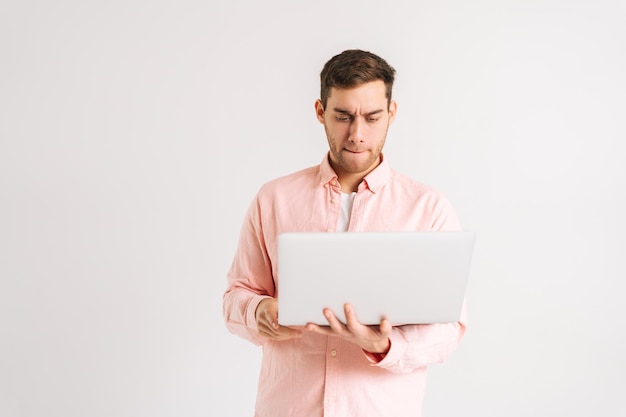 Retrato de jovem sério de pé com laptop e digitando no teclado fazendo trabalho freelance escrevendo e-mail em fundo branco isolado