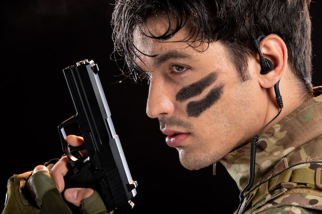 Retrato de jovem soldado camuflado apontando arma na parede preta