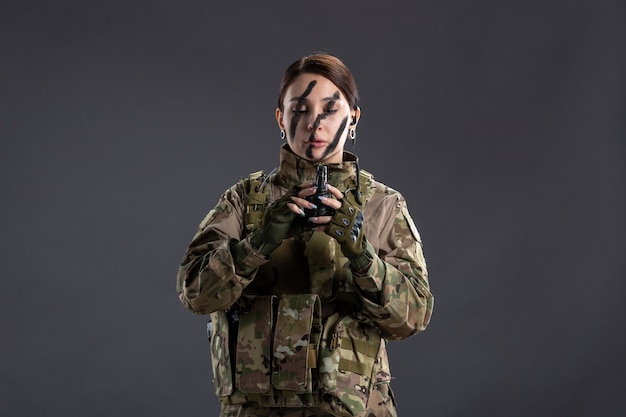 Retrato de jovem soldado camuflado com granada na parede escura de mãos