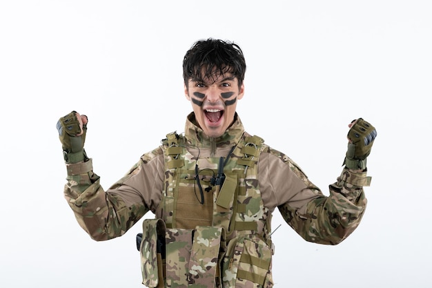 Retrato de jovem soldado camuflado comemorando vitória. Parede branca