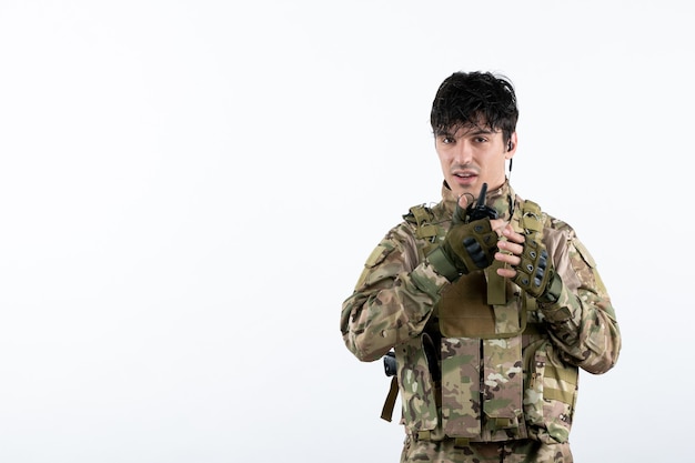 Retrato de jovem soldado camuflado falando através de uma parede branca de walkie-talkie