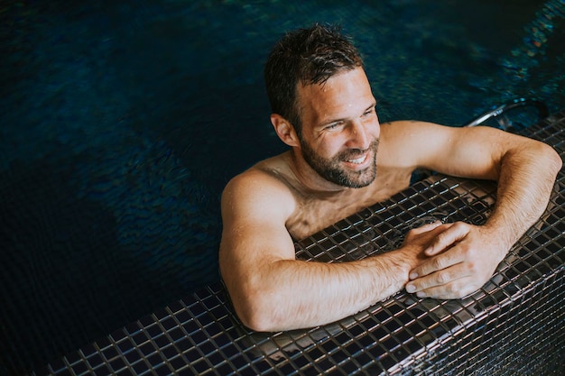 Retrato de jovem sorridente bonito relaxando à beira da piscina