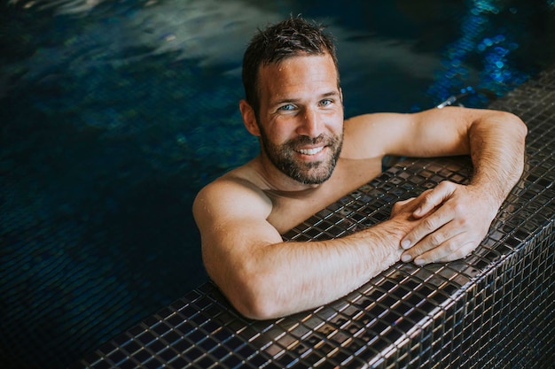 Retrato de jovem sorridente bonito relaxando à beira da piscina