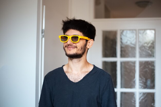 Retrato de jovem sorridente com óculos de sol amarelos.