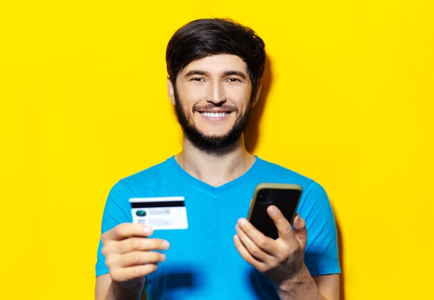 retrato de jovem sorridente de camisa azul usando smartphone e cartão de crédito