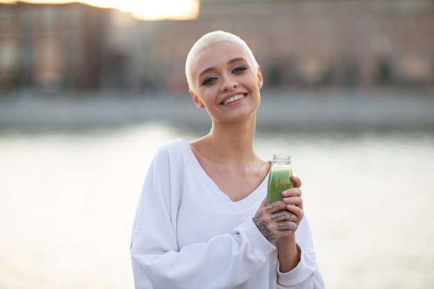 Retrato de jovem sorridente milenar europeu de cabelos curtos com suco verde lindo feliz ...