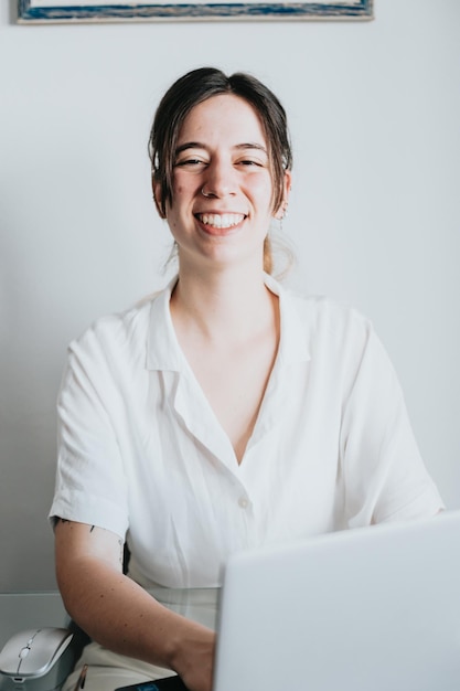 Retrato de jovem sorrindo para a câmera trabalhando em um laptopEmpresária criativa consultando e revisando documentosEntusiasmado e nervoso com o novo empregoescritóriocolegas de trabalho agendas tarefas e tarefas
