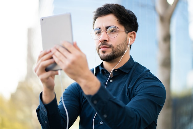 Retrato de jovem tendo uma videochamada em tablet digital em pé ao ar livre. Conceito urbano.