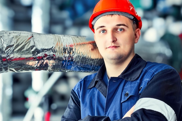 Retrato de jovem trabalhador engenheiro caucasiano no capacete nas instalações da oficina de fábrica