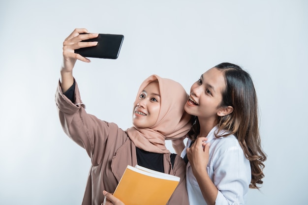 Retrato de jovem universitário feliz carregando uma bolsa e tirando uma selfie com o celular em um branco isolado