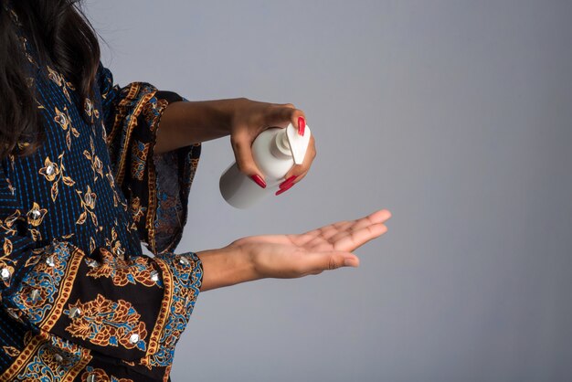 Retrato de jovem usando ou mostrando um gel desinfetante de uma garrafa para limpeza de mãos.