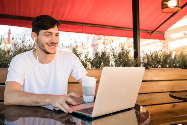 Retrato de jovem usando seu laptop enquanto está sentado em uma cafeteria. Conceito de tecnologia e estilo de vida.