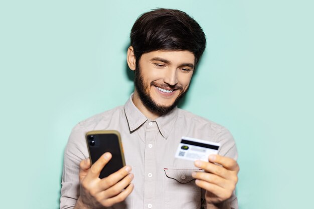 retrato de jovem usando smartphone e cartão de crédito no fundo do aqua menthe