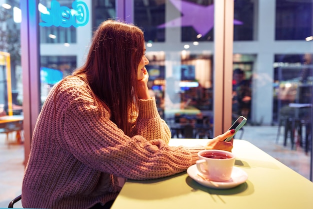 Retrato de jovem usando telefone celular enquanto está sentado em uma cafeteria confortável