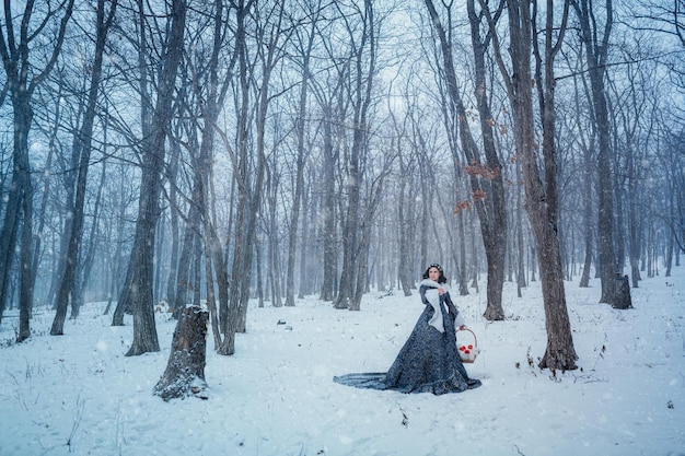 Retrato de jovem vestida com casaco azul. Ela está caminhando na floresta de inverno segurando uma cesta com maçãs