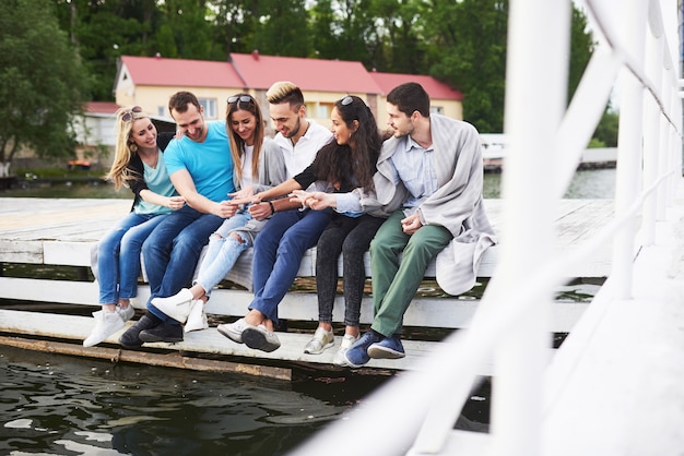 Retrato de jovens amigos felizes, sentado em um píer no lago.