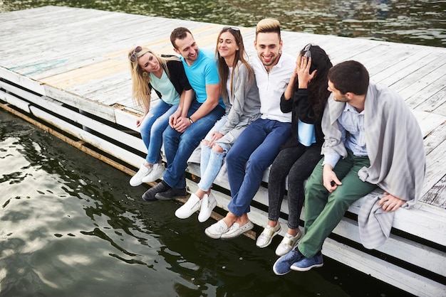Retrato de jovens amigos felizes, sentado em um píer no lago.