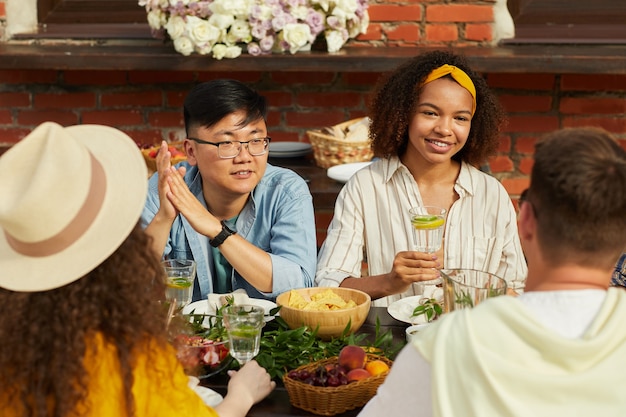 Retrato de jovens desfrutando de um jantar com amigos ao ar livre e segurando coquetéis refrescantes enquanto estão sentados à mesa durante a festa de verão