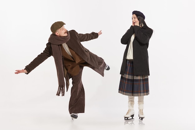 Retrato de jovens elegantes, homem e mulher, se divertindo patinando sobre o inverno de fundo branco